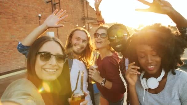 Des amis heureux faisant des selfies drôles et agitant les mains à la fête sur le toit au coucher du soleil. Le fond du mur de briques. L'espace urbain. En plein air. Multi-étatique — Video