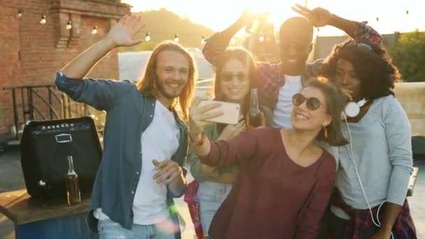 Jovens amigos fazendo selfies engraçadas na festa no terraço ao pôr-do-sol. O fundo da parede de tijolos. Espaço urbano. Ao ar livre. Multi-étnico — Vídeo de Stock