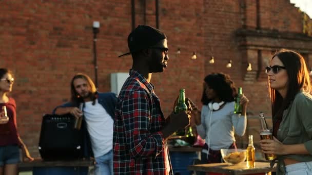 Young man and woman talking and drinking beer at the rooftop party. The brick wall background. Outside. Multiethnical — Stock Video