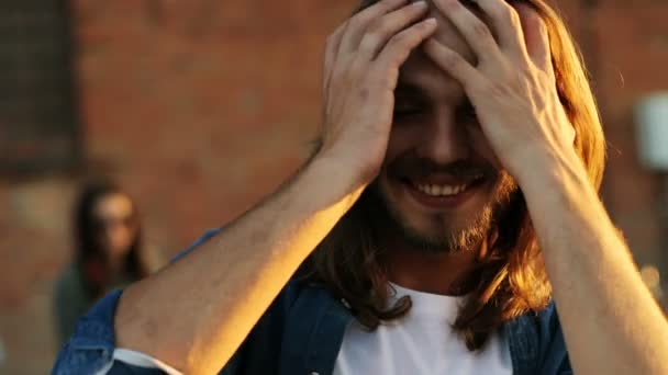 Tiro de perto de homem atraente com cabelo loiro longo na festa no telhado. O fundo da parede de tijolos. Espaço urbano. Lá fora. retrato — Vídeo de Stock