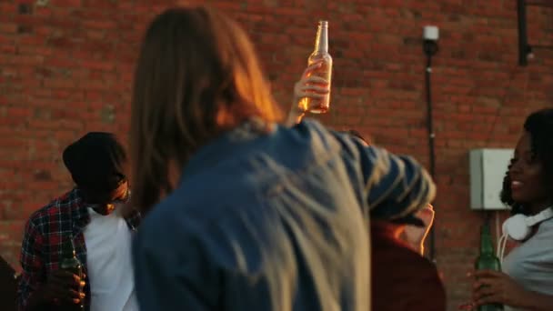 Ein paar junge Freunde tanzen mit Bierflaschen im Kreis auf der Dachparty im Sonnenuntergang. der Backsteinmauer Hintergrund. Draußen. multiethnisch — Stockvideo