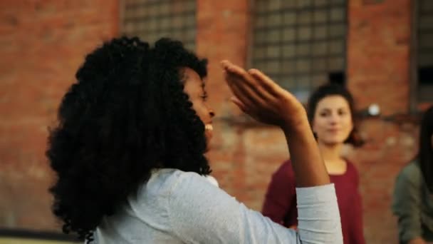 Mujer afroamericana bastante joven que viene a sus amigos en la fiesta de la azotea. El fondo de la pared de ladrillo. Al aire libre. Razas mixtas — Vídeos de Stock