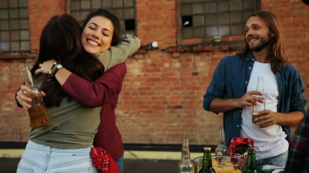 Mujer joven y bonita que viene y da abrazos a sus amigos en la fiesta de la azotea. El fondo de la pared de ladrillo. Al aire libre. Razas mixtas — Vídeos de Stock