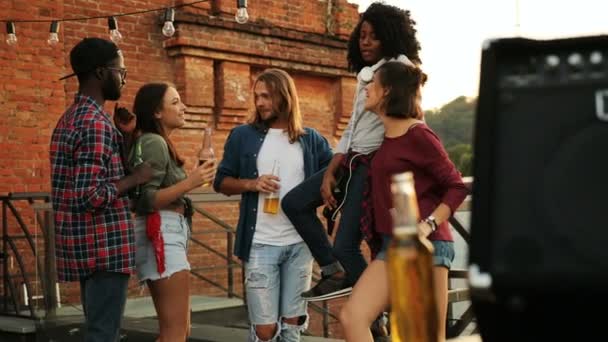 A few young muilti-ethnical friends talking, drinking beer and doing cheers at the rooftop party. The brick wall background. Outdoor. — Stock Video