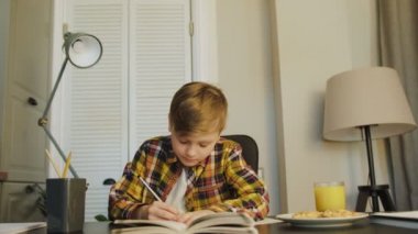 Masada oturan ve ev ödevi içinde defterini yazma iyi çocuk portre çekim zaman babası onu izlemeye gelecek. Meyve suyu ve kurabiye masanın üzerinde. Kapalı