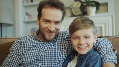 Gülümseyen mutlu baba sakal abd ile portre çekim oturma odasında kanepede oturan sevimli küçük oğlu. Yakın çekim. Poz. Kapalı