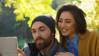 Güneşli ama serin günü parkta tablet cihaza görüntülü sohbet sahip genç çekici çift. Yakın çekim. Portre. Açık havada