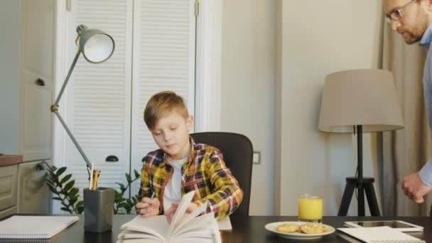 Un écolier faisant ses devoirs au bureau et son père venant le vérifier dans la jolie chambre. Intérieur — Video