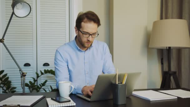 Knappe zakenman in glazen huis werken op de laptopcomputer op de tafel met ernstige gezicht. Gezellige kast. Binnenshuis — Stockvideo