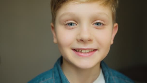 Retrato tiro do menino adolescente loira bonito olhando para a câmera e sorrindo alegremente na frente da câmera. Fecha. Interior — Vídeo de Stock