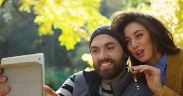 Primer plano de joven sonriente pareja de vídeo charlando en la tableta blanca de la computadora y soplando besos en el parque en el día soleado. Un retrato. Exterior — Vídeo de stock