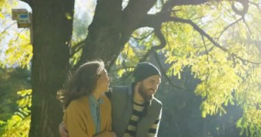 Çekici bir genç adam ve kadın gülüyor ve güneş ışığı altında parkın içinden güneşli sonbahar gününde geziniyor. Dışarıda
