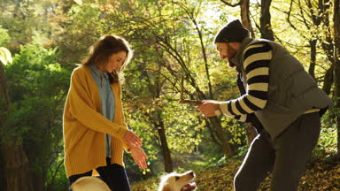 Kadın ve şirin bir köpekle oynamayı ve bir köpek yapma adam atlamak ve bir sopa almak gülüyor. Güneşli bir günde güzel bir sonbahar park. Açık havada