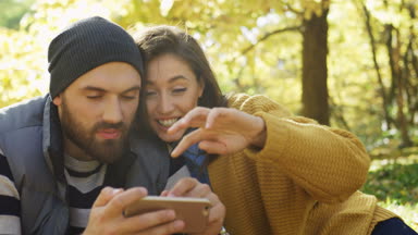 Genç mutlu çiftin akıllı telefon ekrana bakarak ve sonbaharda güzel parkta sarılma kapatın. Güneşli bir gün. Dışarıda