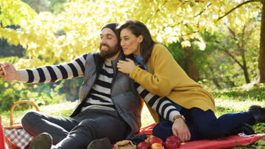 Güneşli sonbahar gününde sarı parkta akıllı telefonda görüntülü sohbet sahip genç çekici çift. Açık