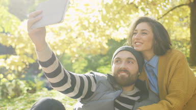 Güneşli havalarda sonbahar parkta tablet cihaza selfies yapma genç çekici çift portre vurdu. Dışarıda