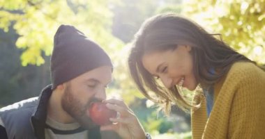 Parkta oturan aşık mutlu genç çiftin yakın çekim. Adam bir elma ve üzüm yemek kadın ısırma. Güneşli sonbahar. Dışarıda. Portre