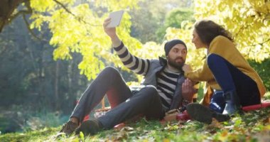 Genç mutlu çift sarı ağaçları arasında sonbahar parkta tablet bilgisayarda güzel selfies yapma. Güneşli bir gün. Açık havada