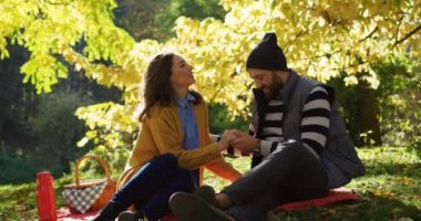 Battaniye çimlerde oturan ve vakit güzel güneşli sonbaharda parkta kadın ve Genç neşeli adam. Onu adam dikkat çekici bir kadın. Açık havada