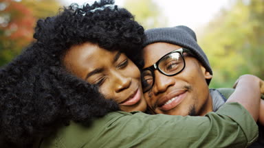 Sarılma ve neşeyle sonbahar parkta kameraya gülme genç çekici Afro-Amerikan çift kapatın. Dışarıda