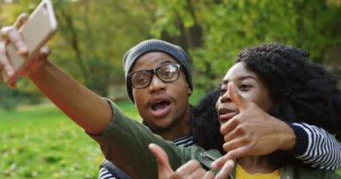 Afrika kökenli Amerikalı çift güneşli havalarda sonbahar parkta akıllı telefonda komik selfies yapma çekici genç kapatın. Açık