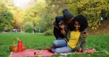 Kırmızı battaniye çimlerde oturan, Öpüşme ve having fun parkta güneşli sonbaharda kadın ve Genç neşeli Afro-Amerikan erkek. Açık havada