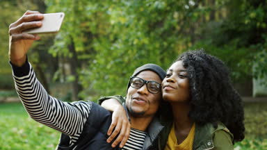 Güneşli bir günde güzel sonbahar parkta akıllı telefon selfies yapma genç çekici Afro-Amerikan çift. Açık