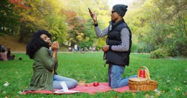 Afrika kökenli Amerikalı çift parkta piknik. Genç adam bir elma ile kıvırcık kadın fotoğrafını çekmek. Sonbahar güneşli gün. Dışarıda