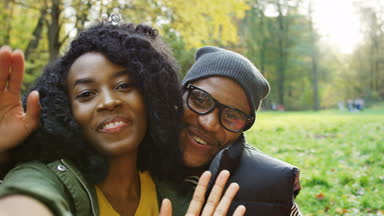 Afrika kökenli Amerikalı çift video sohbet ve sonbaharda güzel parkta ellerini sallayarak gülümseyen genç kapatın. Güneşli havalarda. Açık. Portre. POV