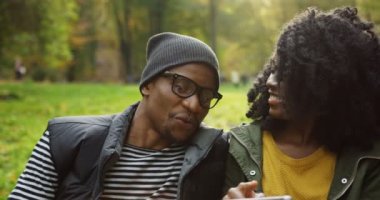 Çiftin birbirine yakın oturan ve ekranda dikkatle baktığını genç çekici Afro-Amerikan kapatın. Portre. Park güneşli sonbaharda. Dışarıda