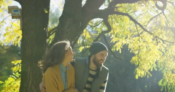 Atractivo joven hombre y mujer riendo y paseando por el parque a la luz del sol en el soleado día de otoño. Afuera. — Vídeo de stock