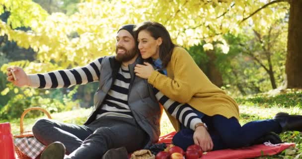 Jonge aantrekkelijke paar videochat gelet op de slimme telefoon in het gele park op zonnige herfstdag. Buiten — Stockvideo