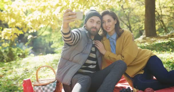 年轻迷人的夫妇在自拍在黄色秋季公园的智能手机上, 在一个晴朗的日子。户外 — 图库视频影像
