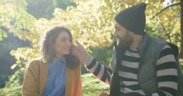 Nahaufnahme eines liebkosen romantischen Paares, das an einem sonnigen Herbsttag im Park sitzt. Porträtaufnahme. Außen — Stockvideo