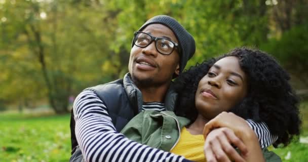 Primer plano de joven pareja afroamericana atractiva en el amor abrazos y el hombre diciendo algo interesante a la mujer. El pintoresco parque de otoño. Al aire libre. Retrato plano — Vídeos de Stock