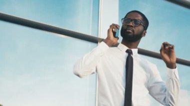 Bir kravat ve akıllı telefonda konuşurken ve büyük pencere arka planını boynuna kadar ısınma gözlük çekici bir Afrikalı-Amerikalı adam. Büyük ofis binası dışında iş adamı.
