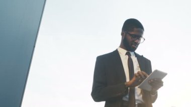 Bir kravat ve onun tablet cihaz dokunarak gözlük yakışıklı Afrikalı-Amerikalı iş adamı. Beyaz gökyüzü arka plan. Açık