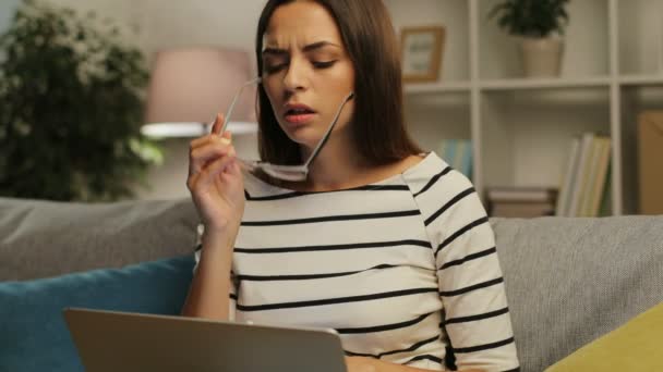 Porträt einer traurigen jungen Frau mit Brille, die am Laptop arbeitet und abends schreckliche Kopfschmerzen zu Hause im Wohnzimmer hat. — Stockvideo