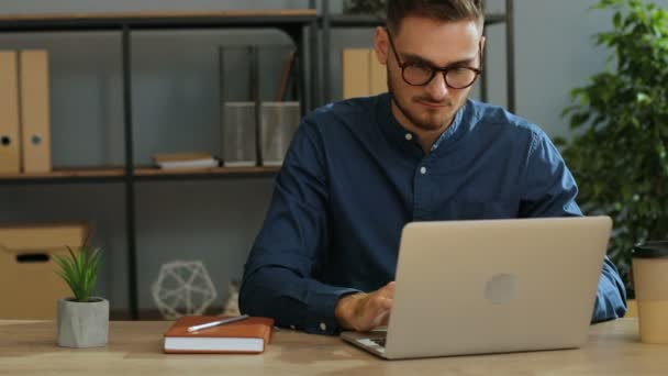 Porträtt av allvarlig ung affärsman i glas arbetar på bärbar dator i det moderna kontoret. — Stockvideo