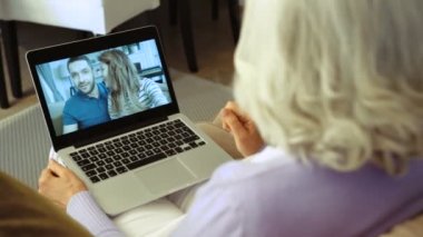 Yaşlı kadın evde oturma odasında video sohbet için dizüstü bilgisayar kullanarak çekim kapatın. Arkadan görüntülemek.