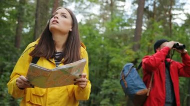 Ormanın içinde kaybolmuş ve harita ve dürbün geri ile bir yardım yolu görünümlü almak sırt çantaları ile genç çift. Dışarıda