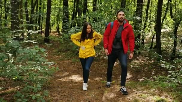 Fiatal pár, séta az erdőben, a hátizsák. Nő, miután egy hátfájás és stoping fáradt. A szabadban — Stock videók