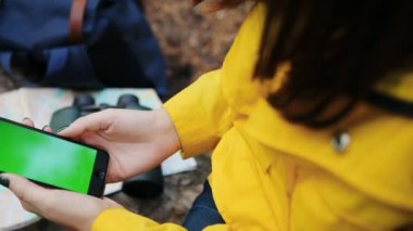 Ormanın içinde akıllı telefon ekrandaki kaydırma el ile kapatın. harita, dürbün ve sırt çantası üzerinde arka plan bulanık. Yeşil ekran. Chroma anahtar. Açık havada
