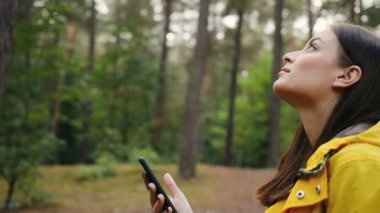 Genç Sevimli Kadın ararken ve tüm çevresinde ve onun akıllı telefon orta ormanın içinde kaydırma daha yakın. Portre vurdu. Açık