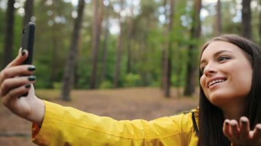 Belgili tanımlık smartphone üzerinde video sohbet ve güzel ormanda elini sallayarak sahip genç güzel kadın portre vurdu. Yakın çekim. Dışarıda