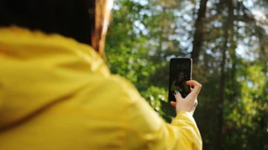 Genç kadının güneşli havalarda siyah smartphone ormandaki selfies yapma kapatın. Arka. Açık havada
