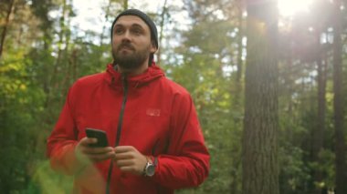 Elinde siyah bir akıllı telefon ile ormanda yürüyüş ve etrafa bir yakışıklı uzun yürüyüşe çıkan kimse portre vurdu. Yakın çekim. Dışarıda