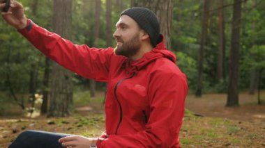 Güzel ormanda oturan ve selfies akıllı telefonundan yapım bir sakallı sportif yakışıklı adam portresi. Açık havada