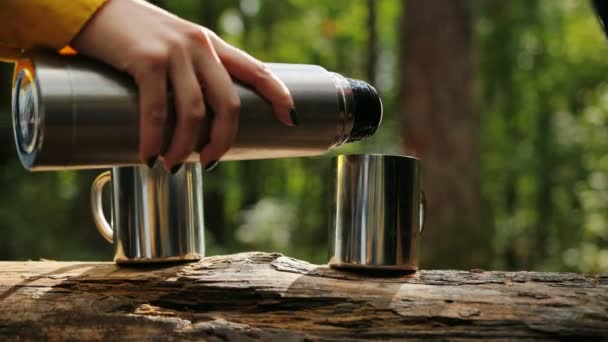 Close up of the female hand pouring a tea from a thermos in the cups which being holded by male hand. Forest background. Outside — Stock Video