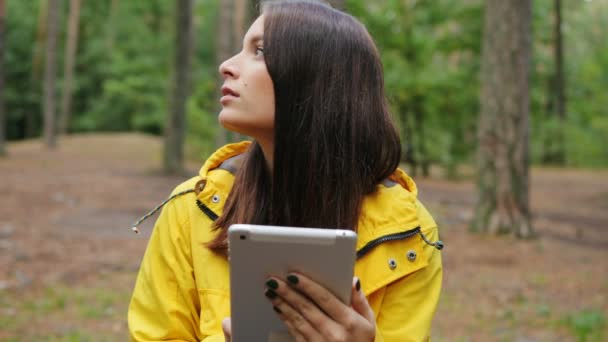 Porträtt av charmiga ung kvinna sitter i skogen, tejpning på sin handdator och tittar runt henne. Vandring ensam. Utanför. Närbild — Stockvideo